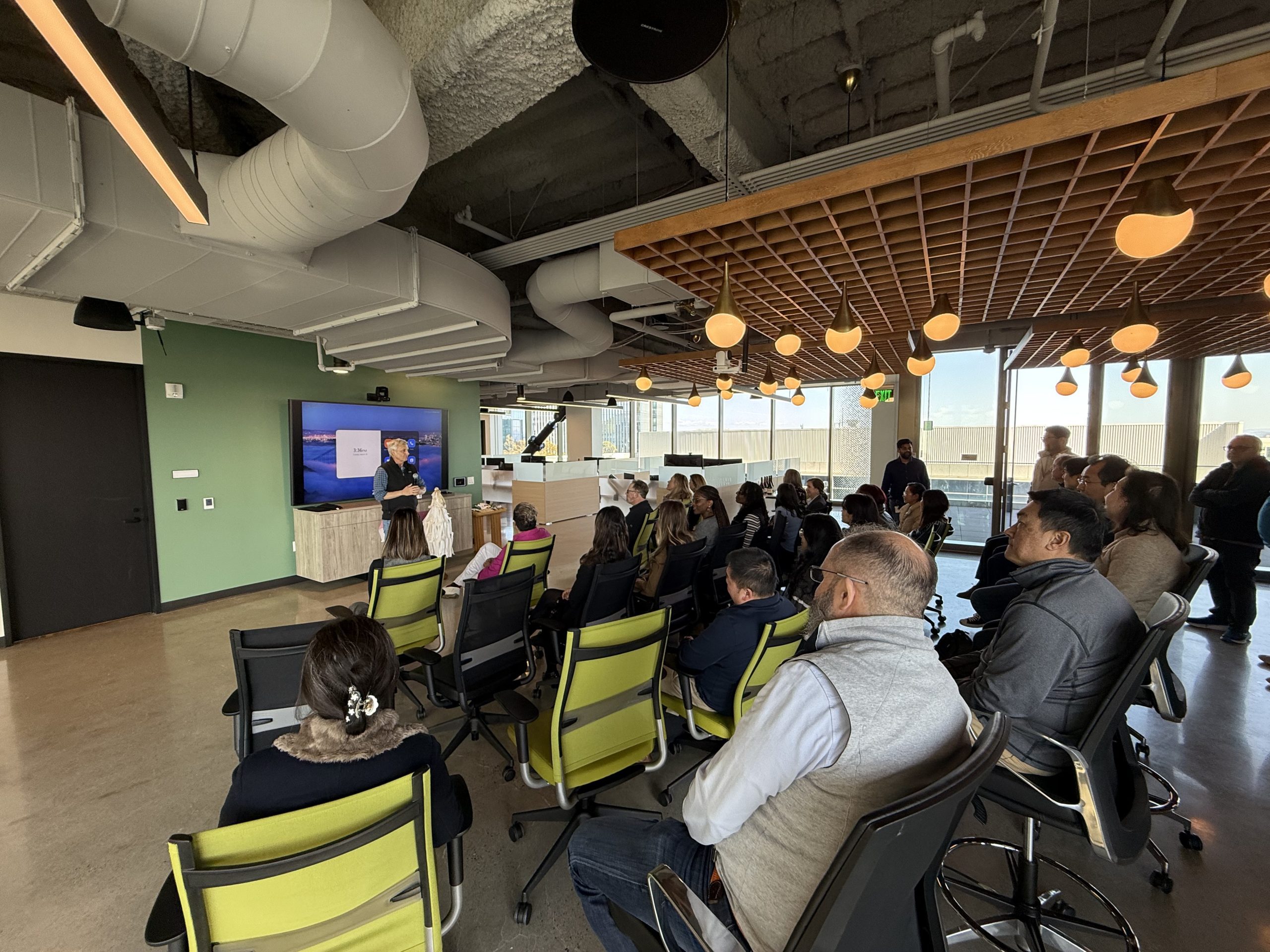 Structure Therapeutics employees sit in a modern office space, watching a presenter stand next to a large digital screen.