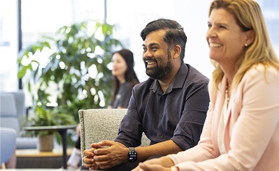Two Structure Therapeutics team members sit side-by-side and look off-camera with smiling expressions in a bright indoor setting.
